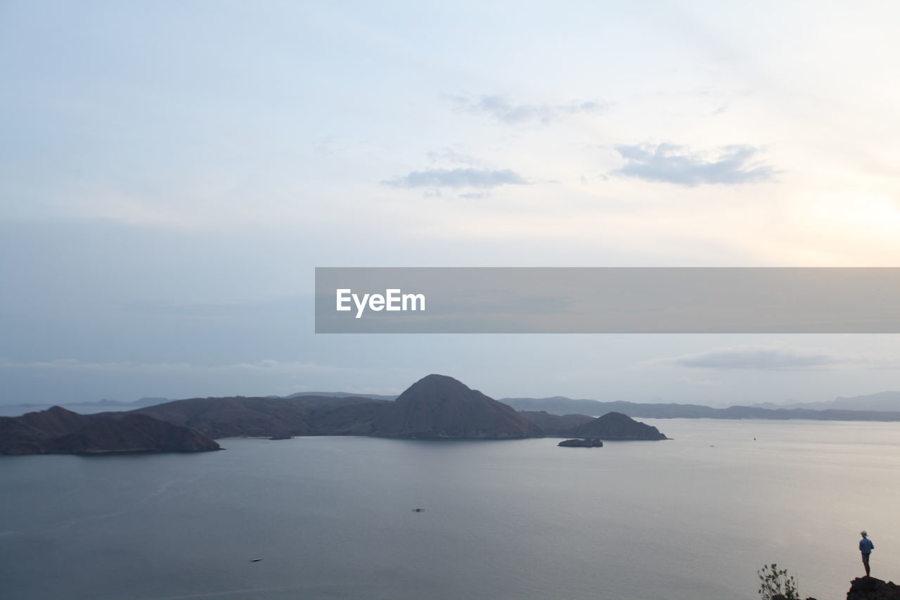 Mid distance view of man standing on cliff by sea against sky