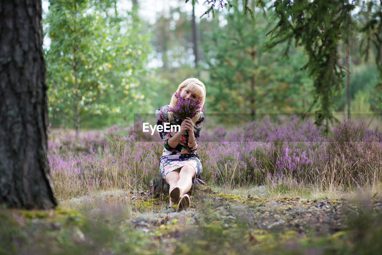 Woman looking away while holding flowers in forest