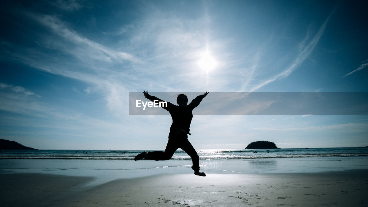 Full length of silhouette woman jumping at beach against sky
