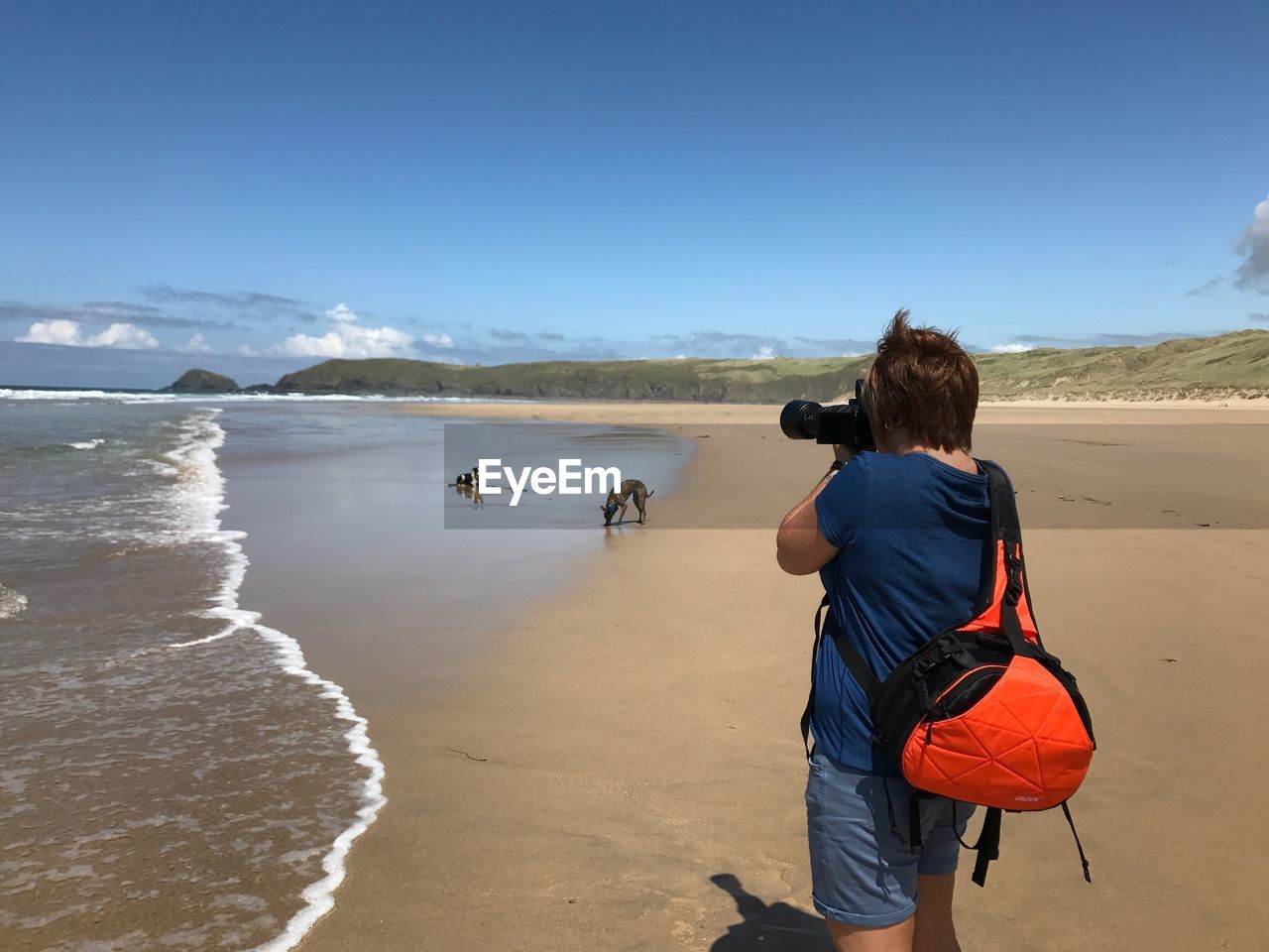 Rear view of woman standing on beach against clear sky holding a camera 