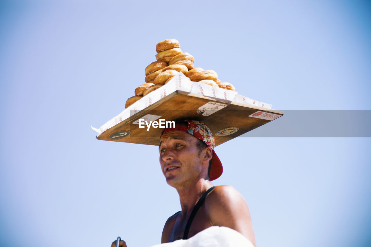 Man balancing tray of bread against clear sky