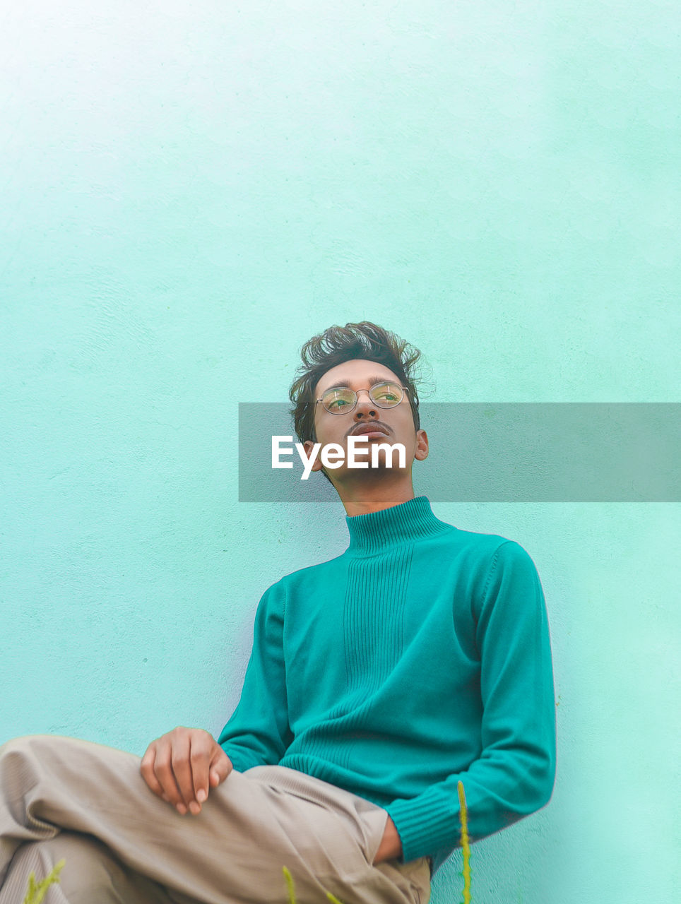 Thoughtful young man sitting against wall