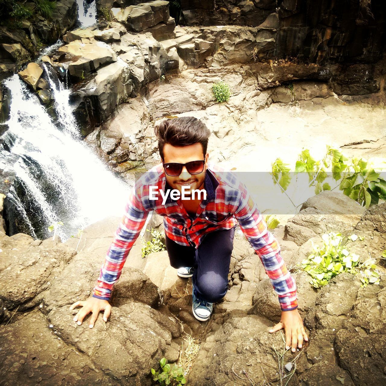 High angle portrait of man climbing on rocks against waterfall