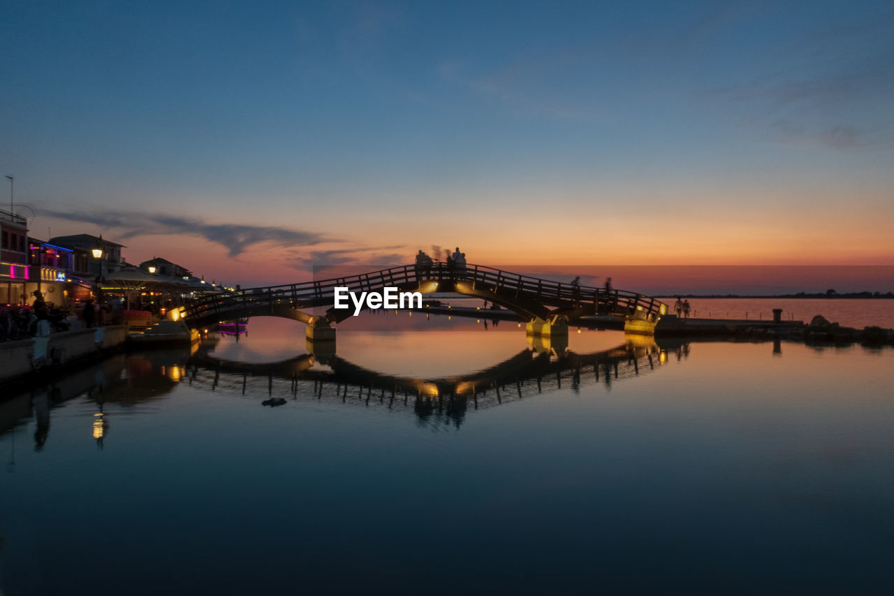 Illuminated bridge over river against sky at sunset