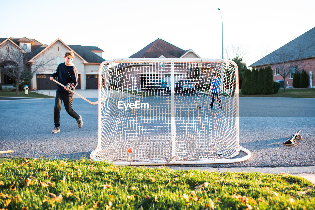 Two boys playing street hockey on a residential street in the fall.