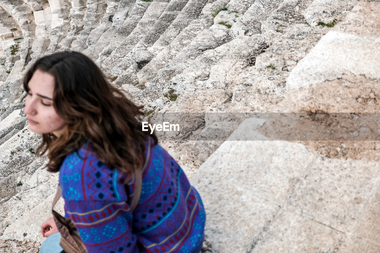 one person, women, leisure activity, adult, casual clothing, day, lifestyles, blue, long hair, hairstyle, nature, looking, female, side view, outdoors, person, high angle view, clothing, brown hair, young adult, rock, wall - building feature, standing, waist up, wall, dress, spring, child, looking away, portrait, pattern