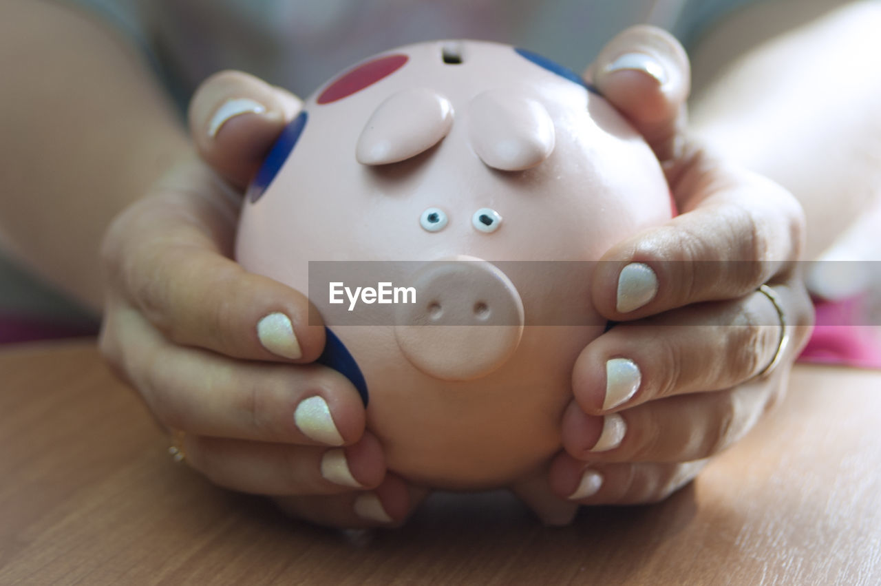 Close-up of hands holding piggy bank on table