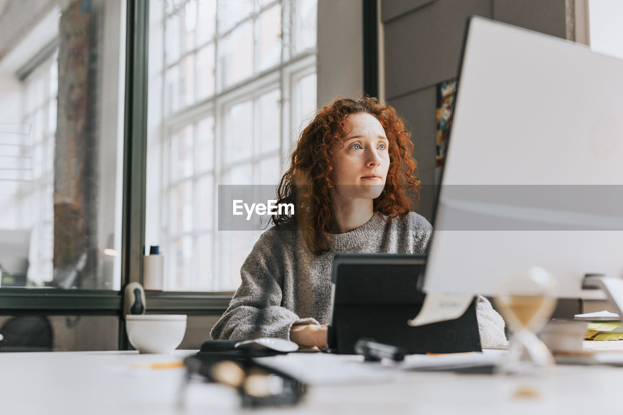 Focused redhead businesswoman working on desktop pc at office