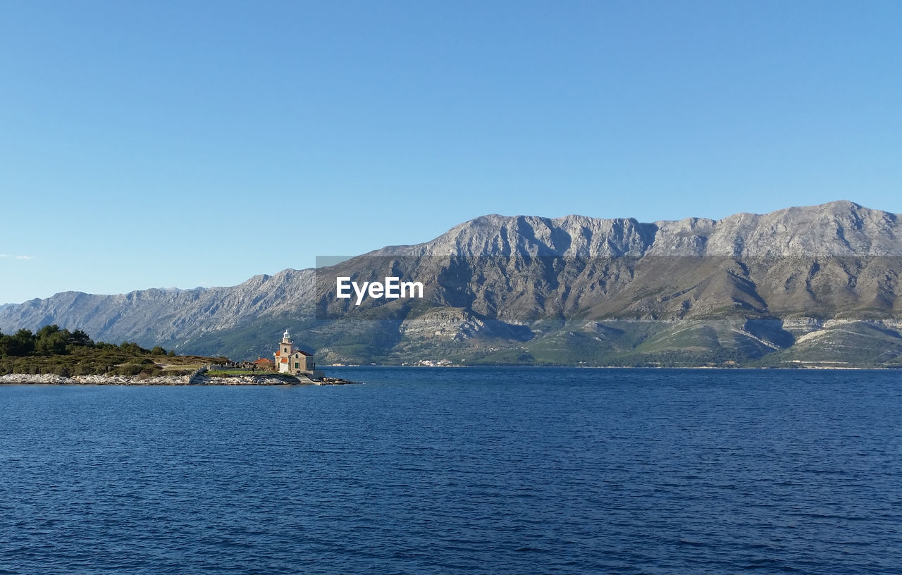 Scenic view of sea and mountains against clear blue sky