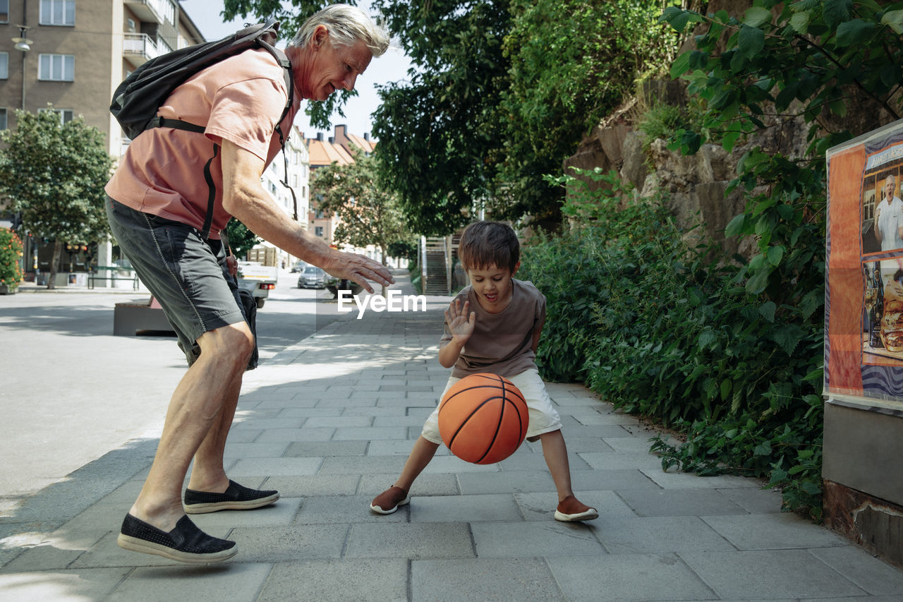 Grandfather playing basketball with grandson on sidewalk