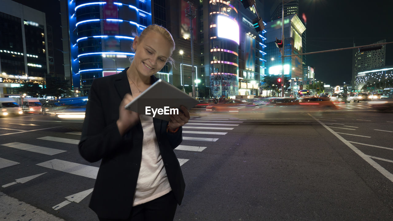 Woman using digital tablet while standing on road in city