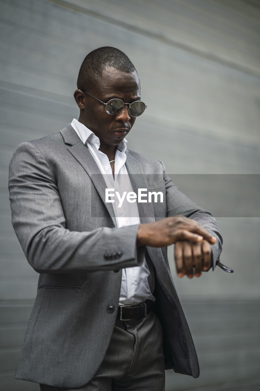 Masculine african american male executive in formal suit and sunglasses revising time on street