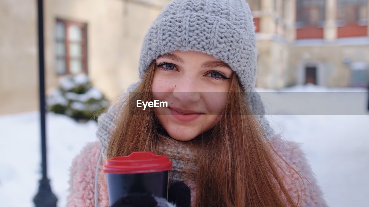 Portrait of young woman holding coffee cup while standing outdoors