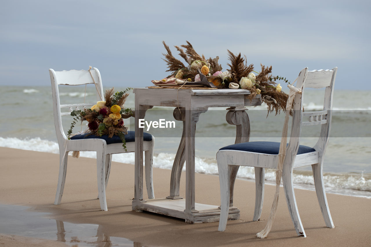 WOODEN TABLE AND CHAIRS ON BEACH AGAINST SEA
