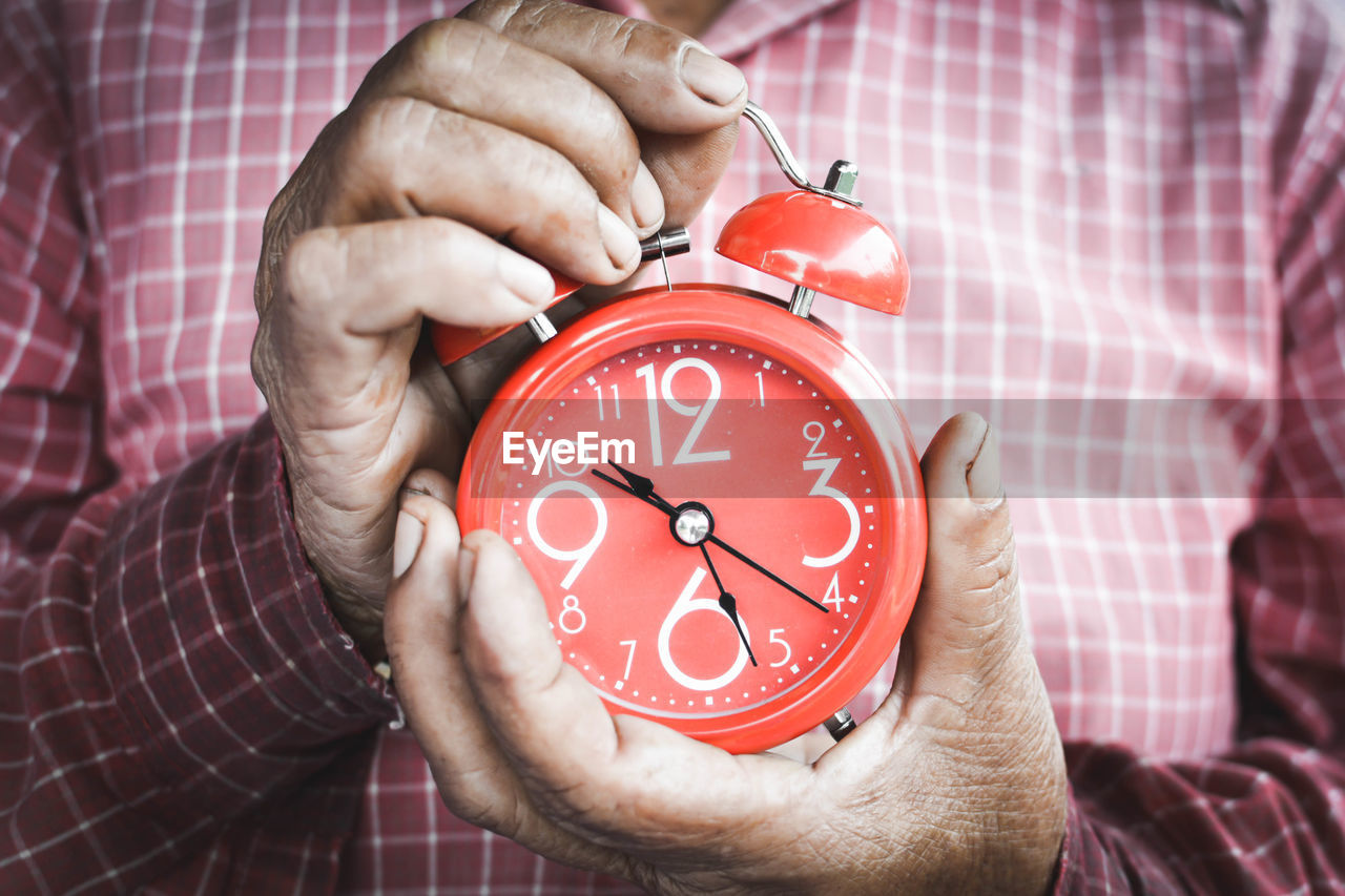 Midsection of man holding red alarm clock