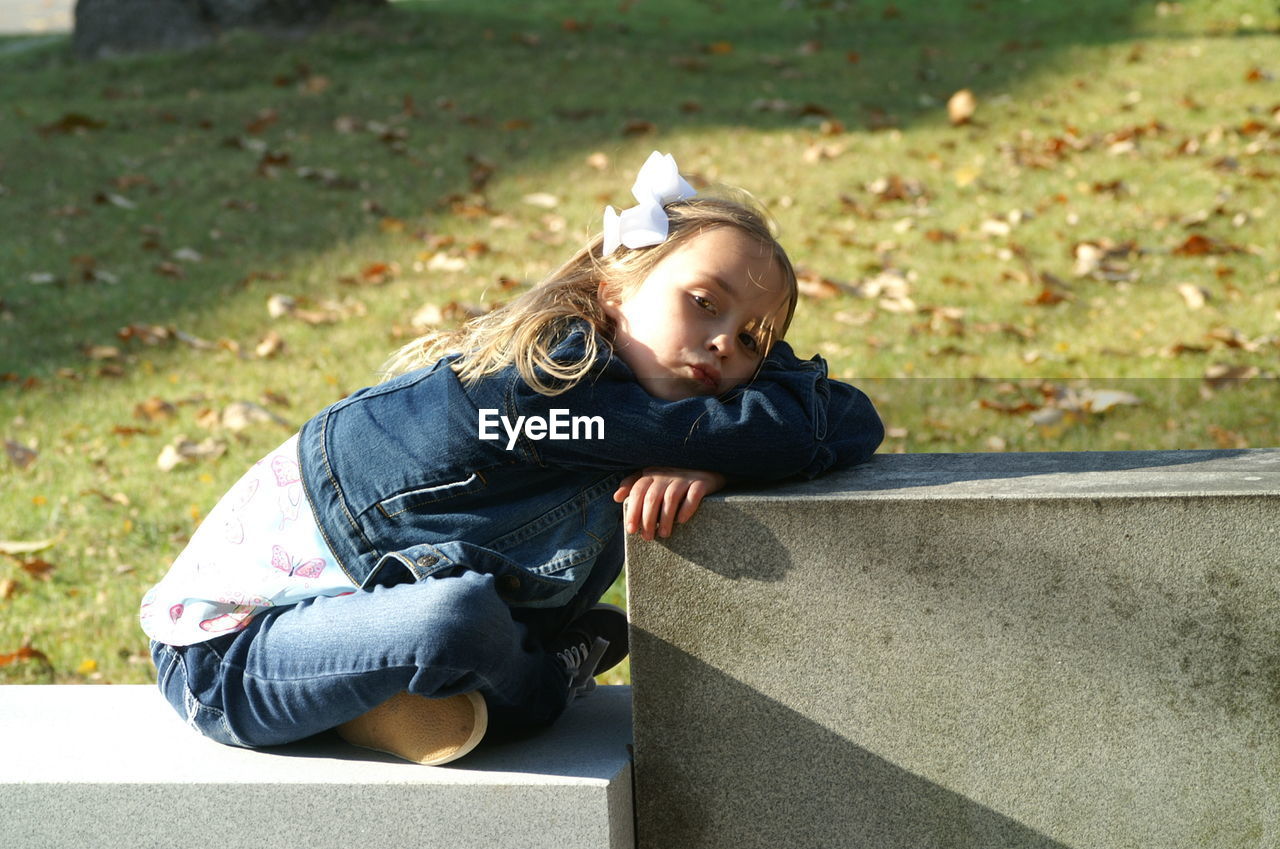 Side view portrait of girl sitting on retaining wall at park