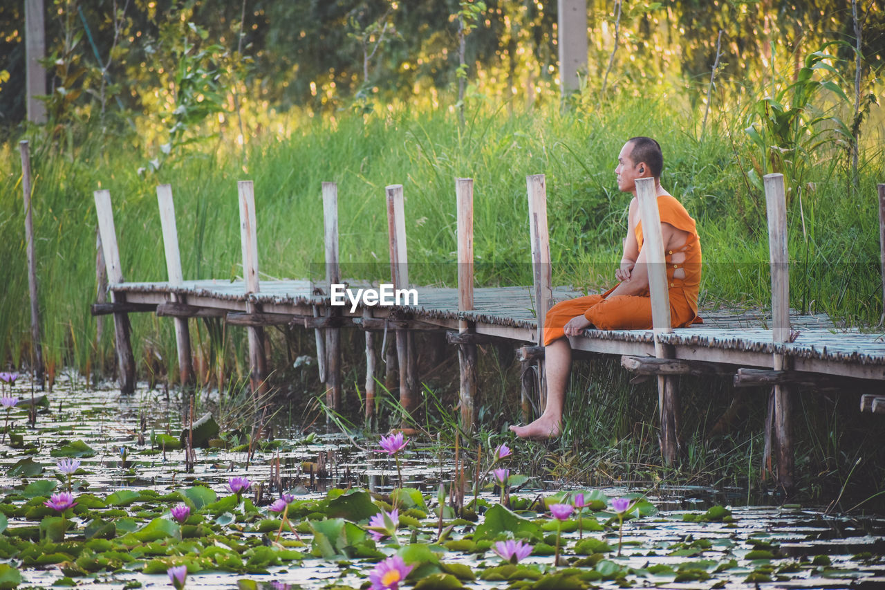 SIDE VIEW OF WOMAN SITTING ON GRASS BY LAKE