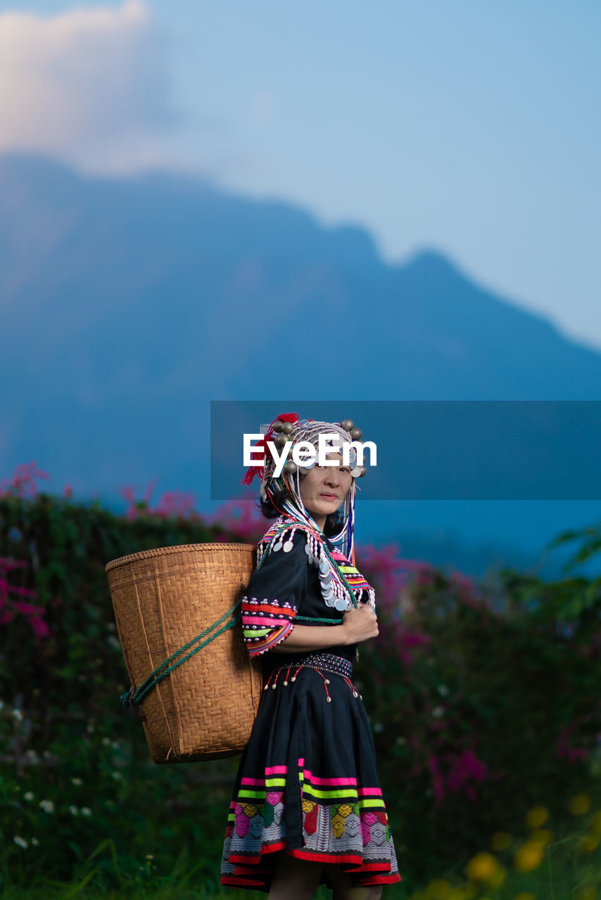 Portrait of smiling woman in traditional clothing holding wicker basket while standing in farm