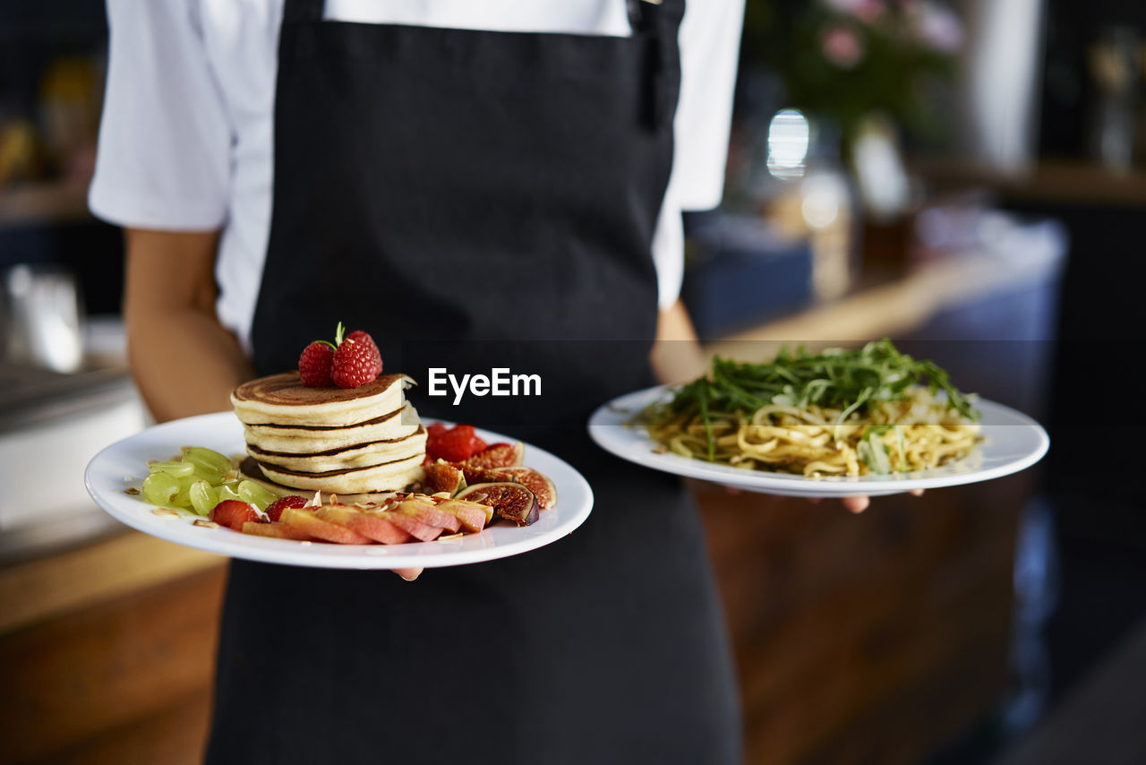 Midsection of female barista holding food plate in coffee shop