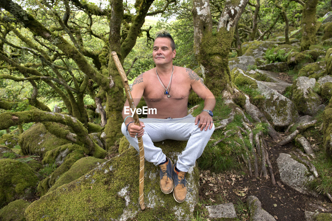 PORTRAIT OF MAN SITTING ON TREE TRUNK