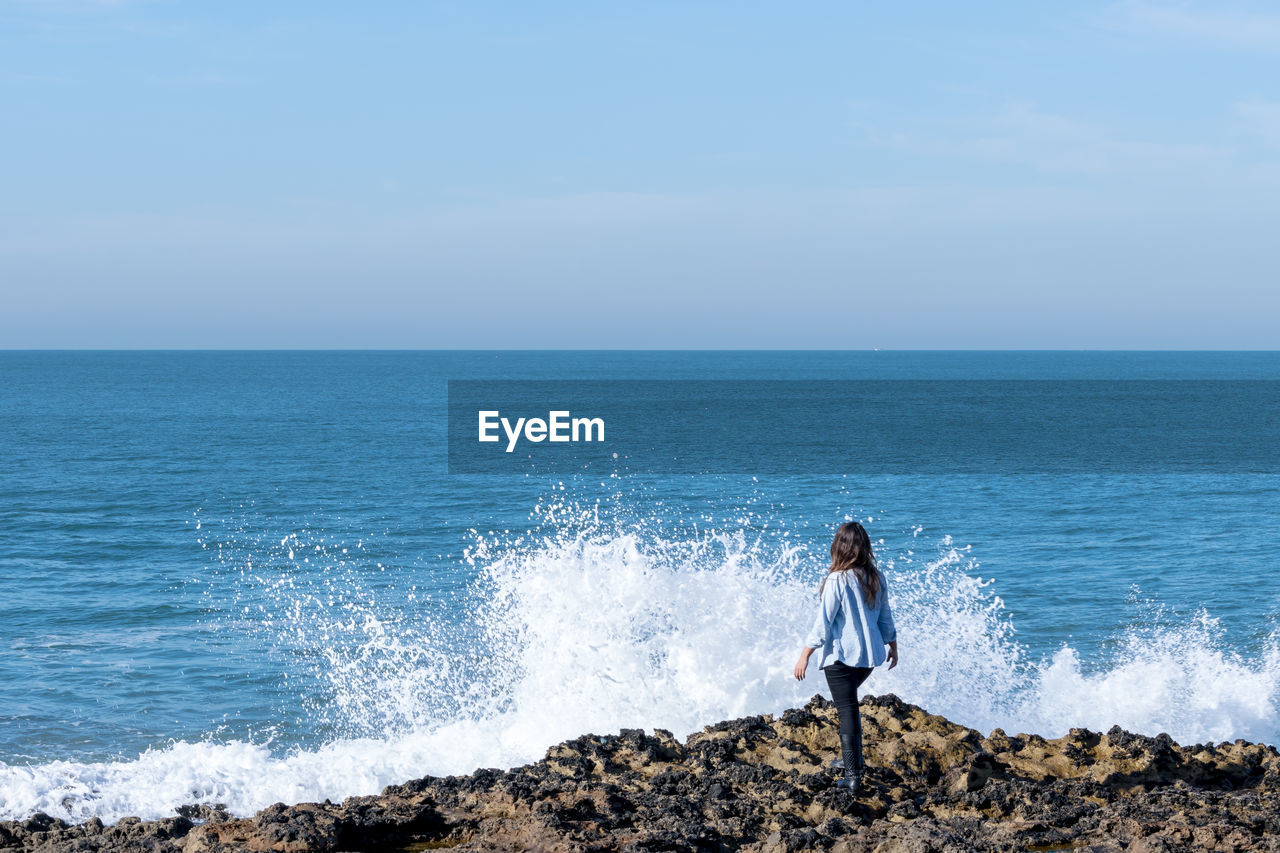 Rear view of woman standing on shore against sky