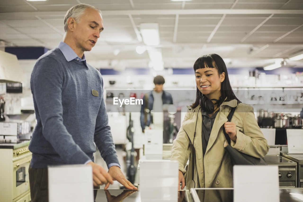 Mature owner talking to smiling female customer in electronics store