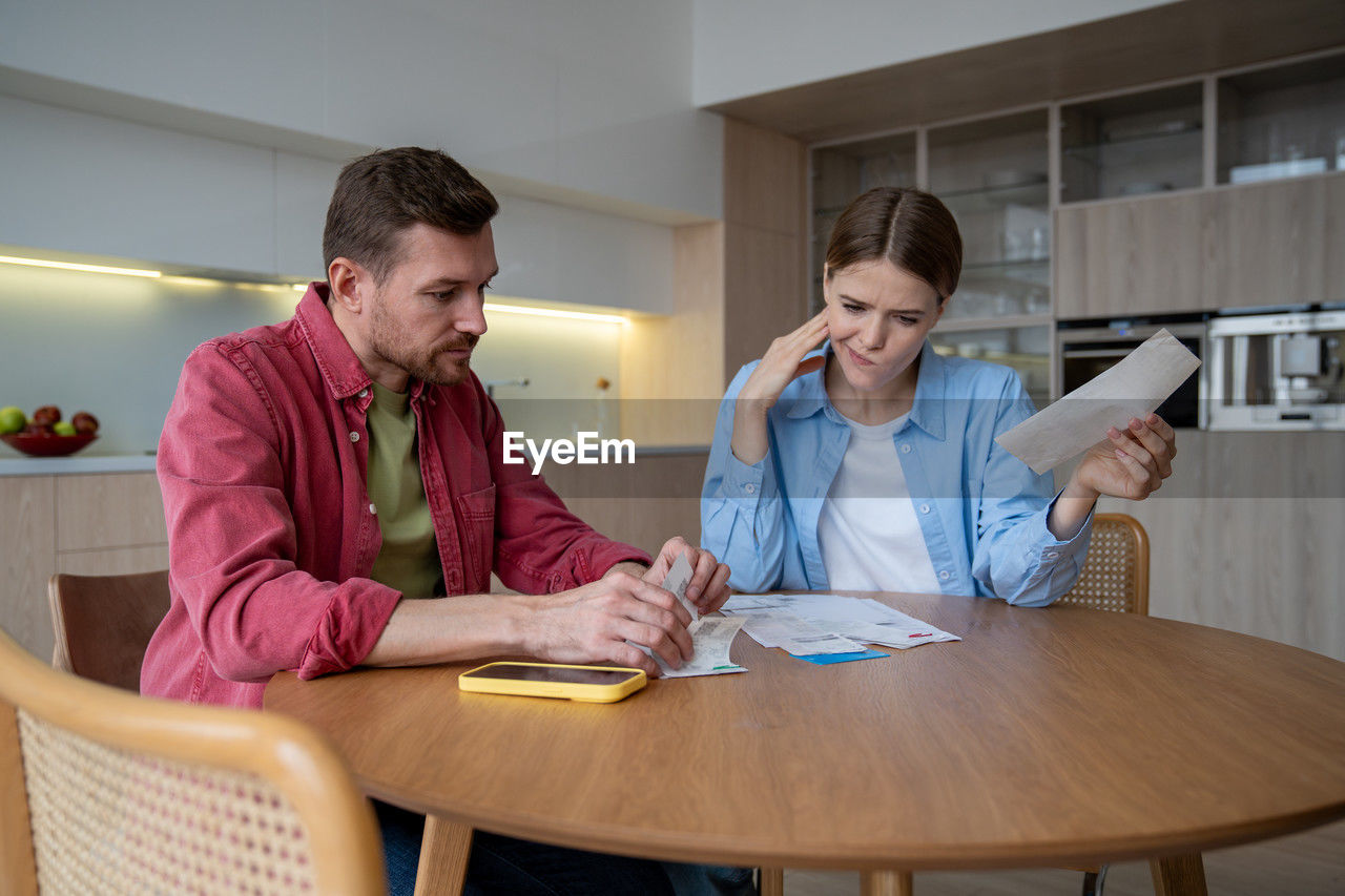 young woman using mobile phone while sitting on table at home