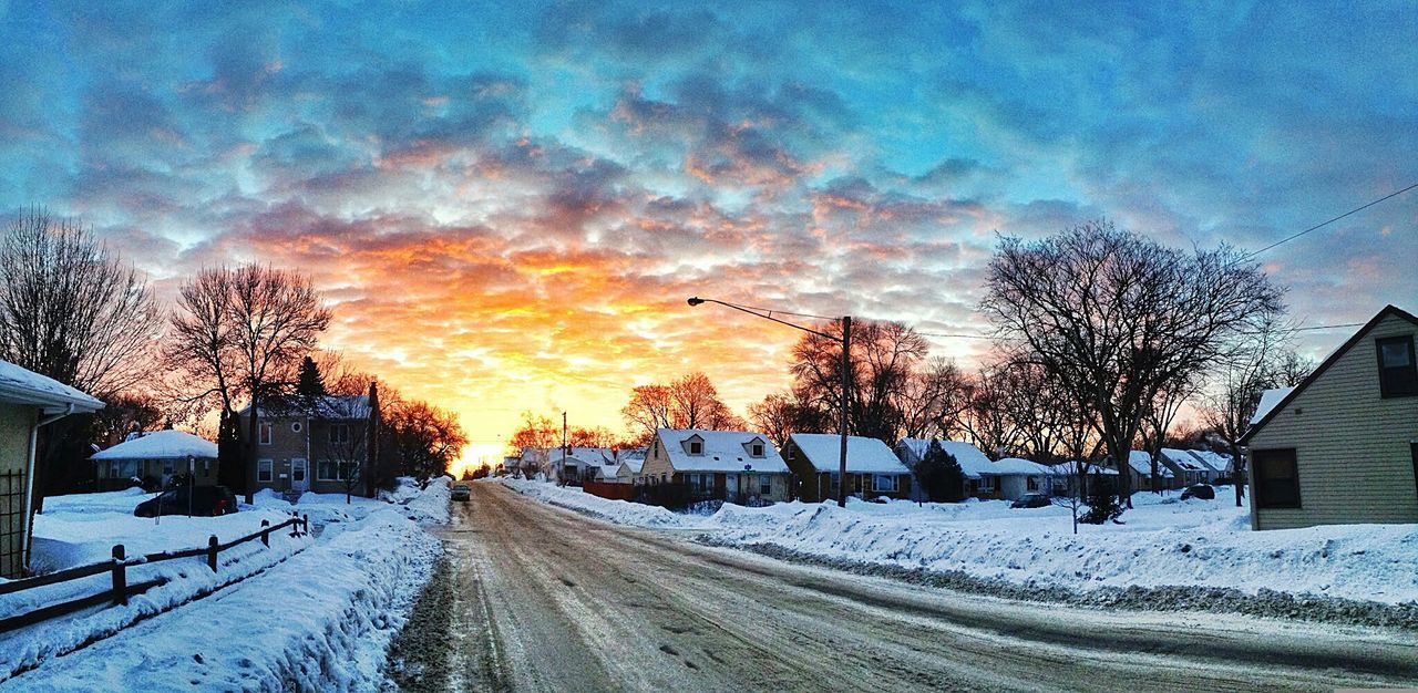 Road amidst snow covered houses against sky during sunset