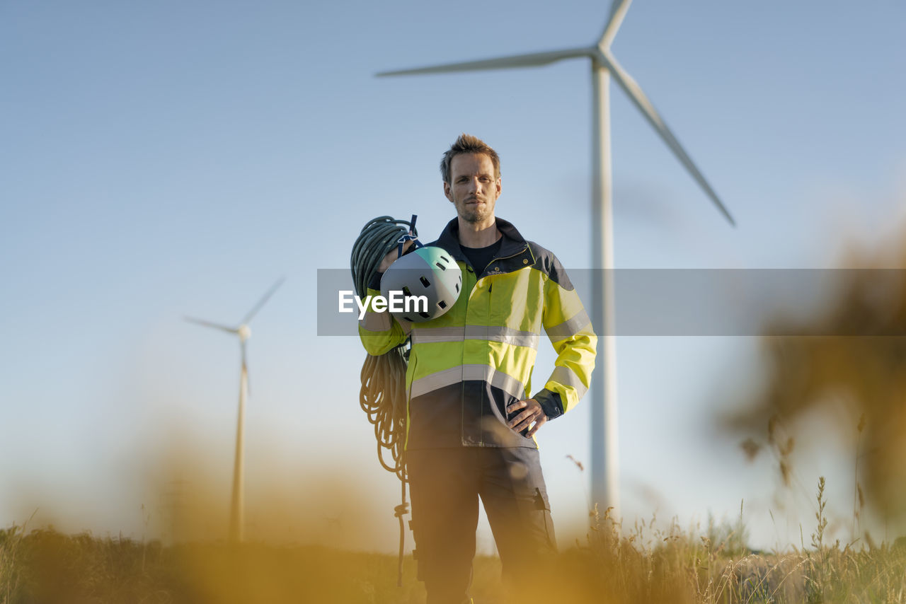 Technician standing in a field at a wind farm with climbing equipment