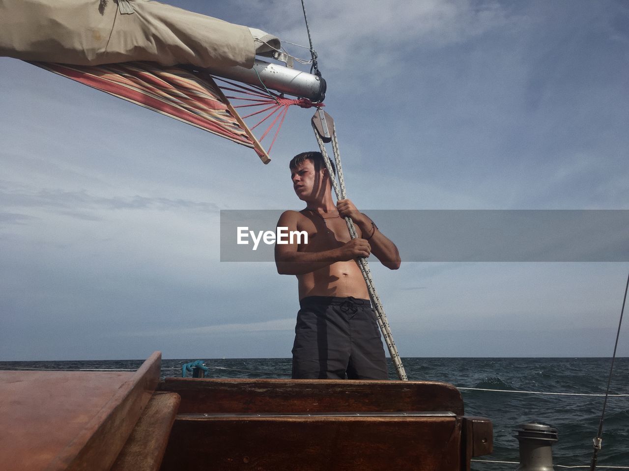 Man holding rope while standing on sailboat in sea against sky