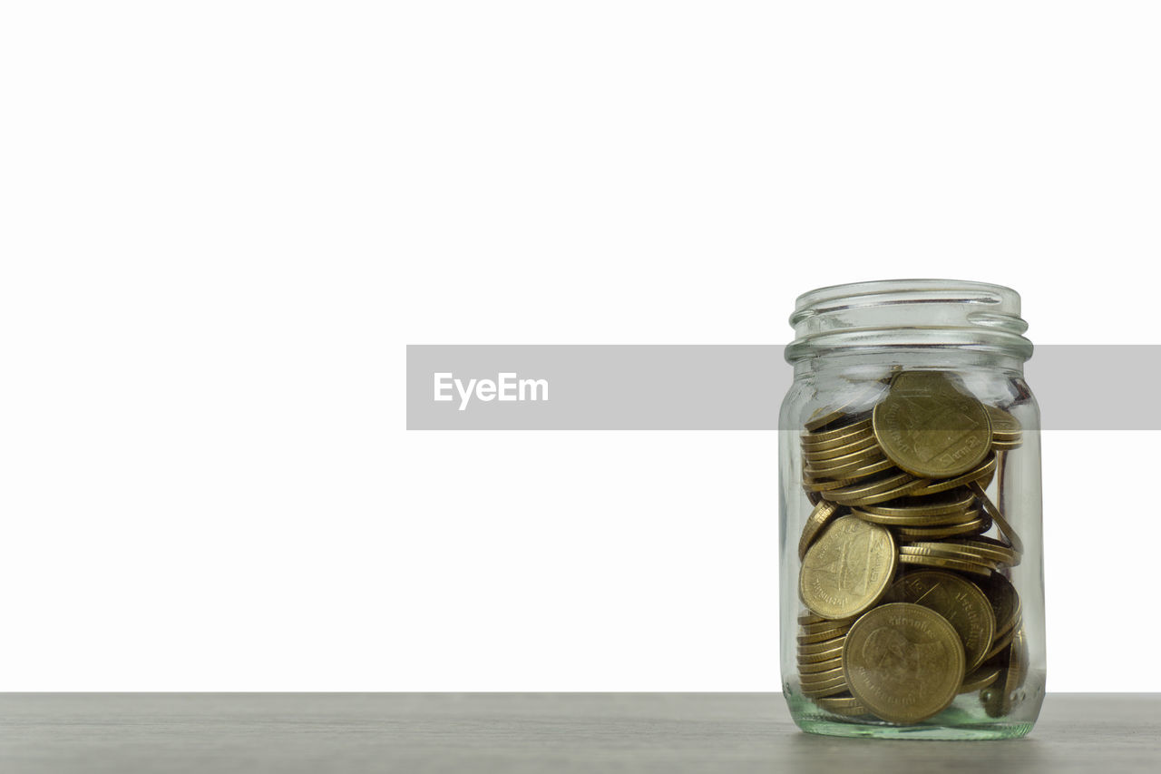 Close-up of coins in jar on table against white background