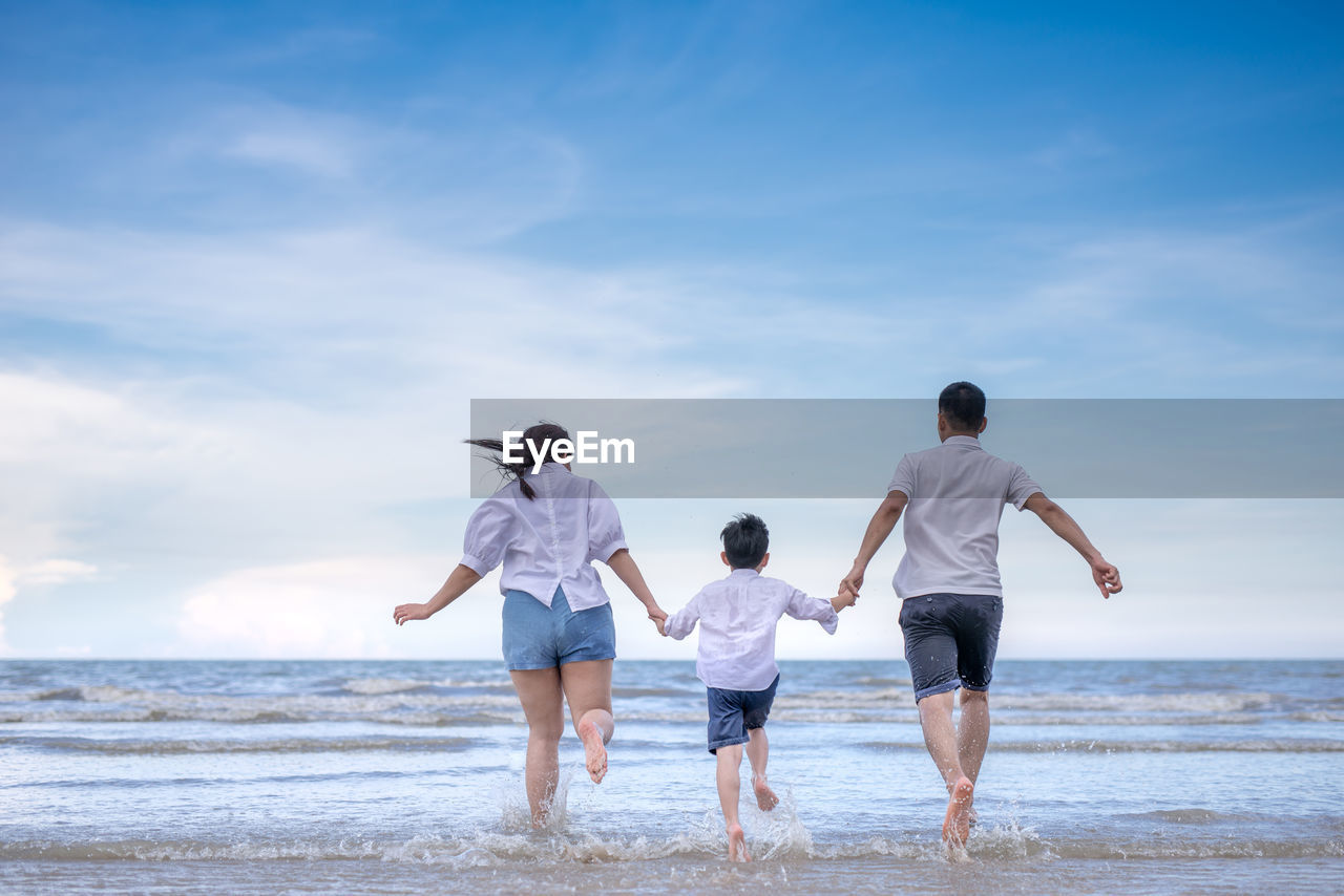 Happy family enjoying at beach against sky