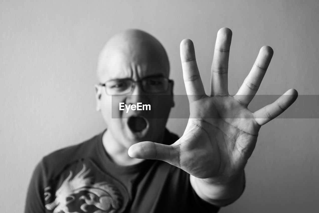 Portrait of angry bald man showing hand while shouting against wall