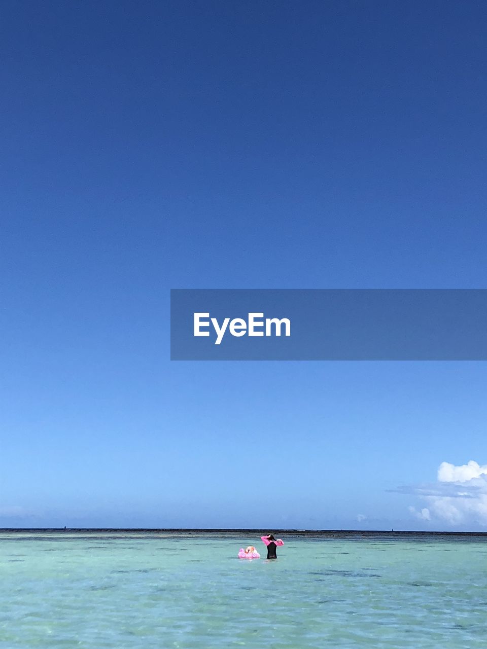 Rear view of woman standing with baby in inflatable pool raft at sea against sky