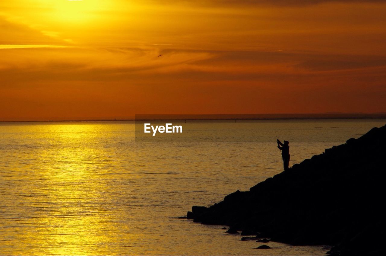 A man fishing on a rock outcrop at dusk