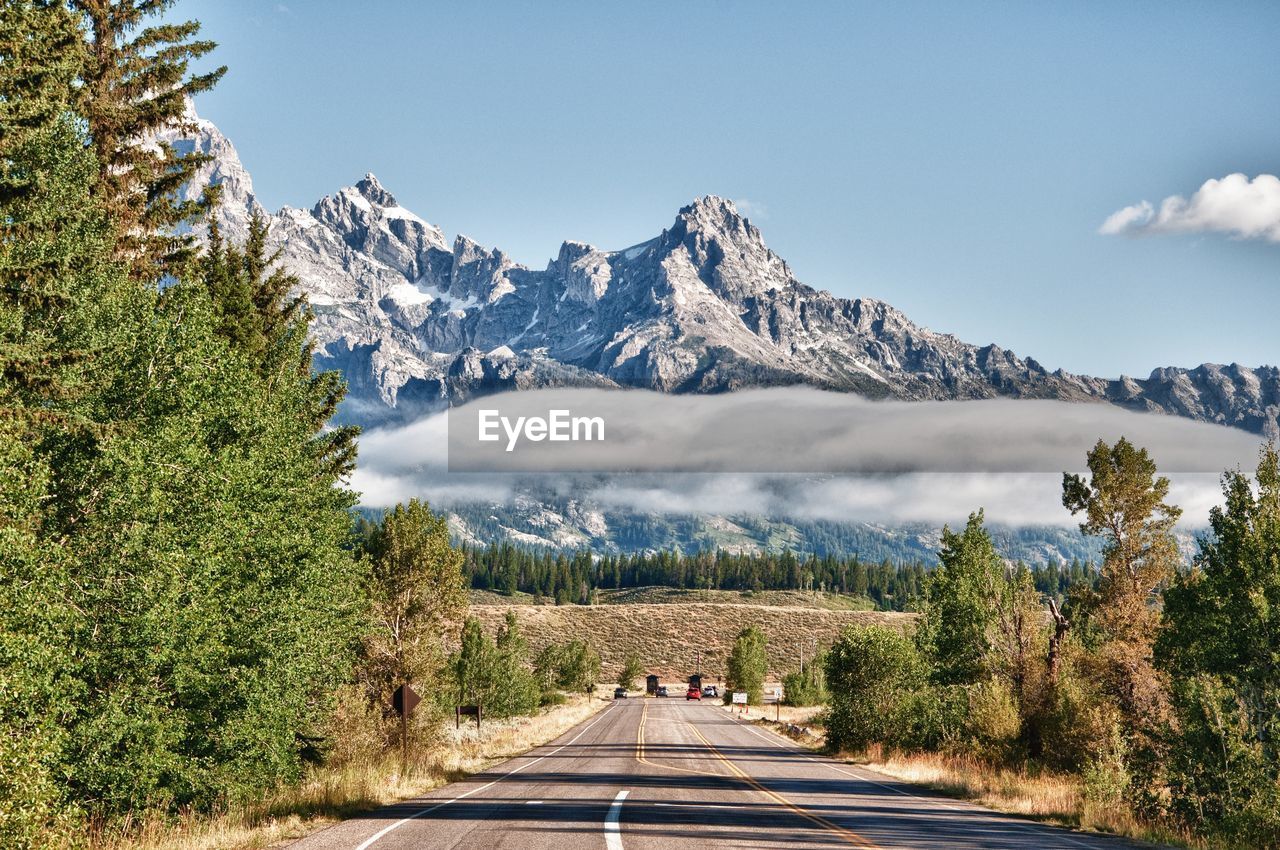 Road amidst trees and snowcapped mountains against sky