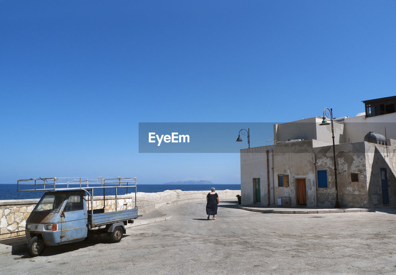 REAR VIEW OF MAN ON ROAD AGAINST CLEAR SKY