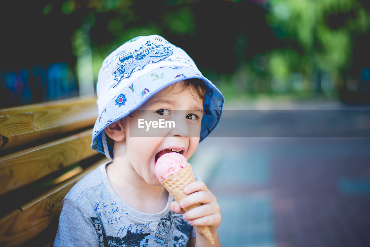 Portrait of cheerful boy eating ice cream while sitting on park bench