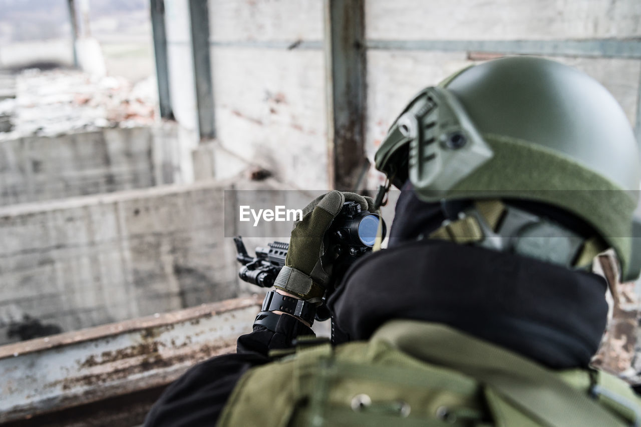 Close-up of army soldier aiming rifle while standing in building