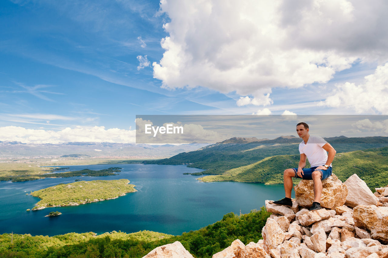 Man sitting on rock at lake against sky