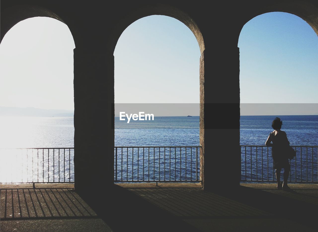 Full length rear view of woman standing by railing against sea