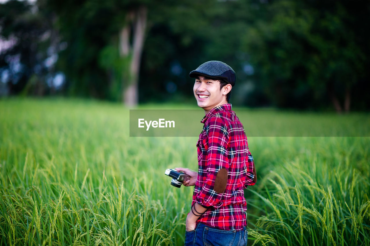 PORTRAIT OF SMILING WOMAN STANDING ON FIELD