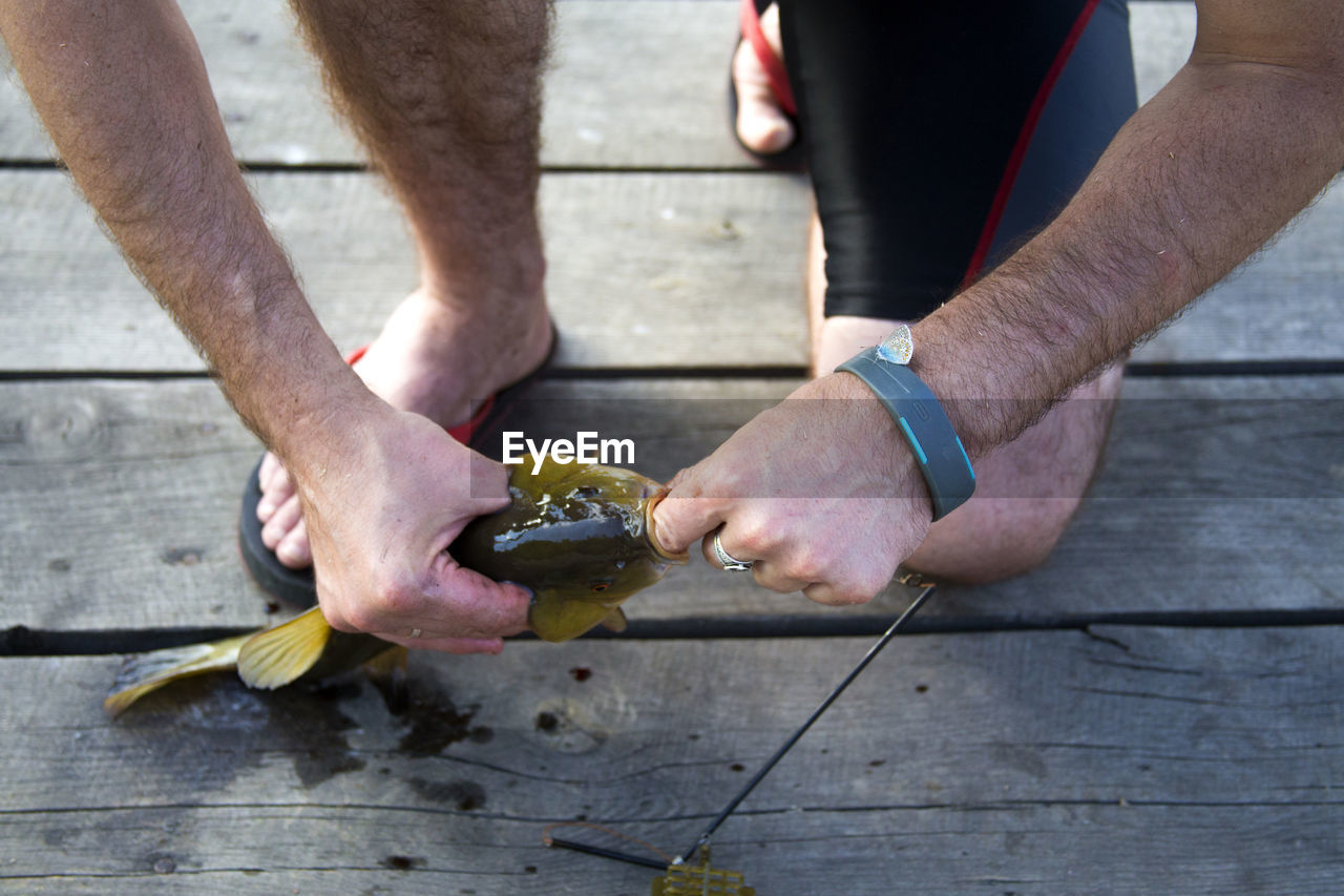 Low section of man holding fish while kneeling on pier