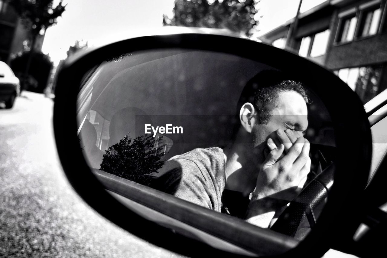 Young man with hands covering mouth reflecting on side-view mirror