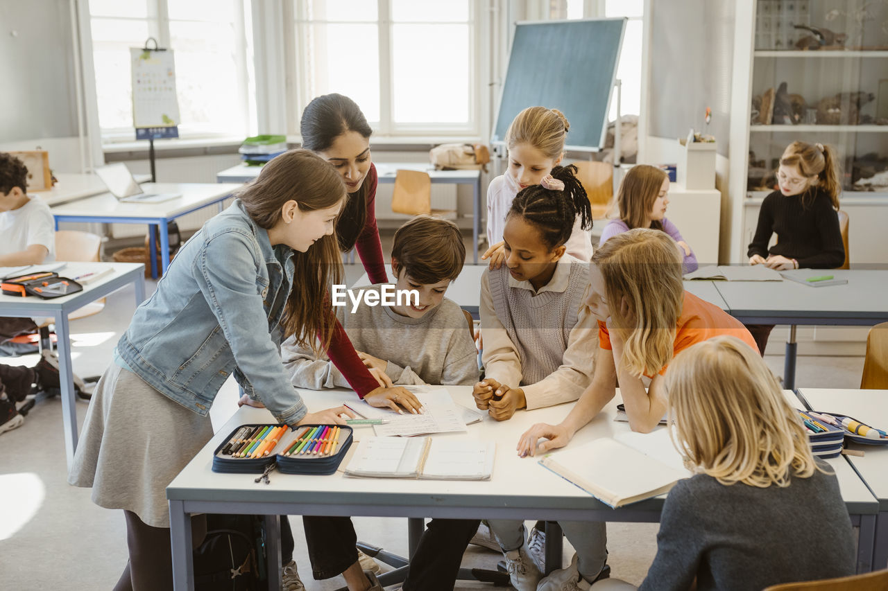 Teacher explaining multiracial students at desk in classroom