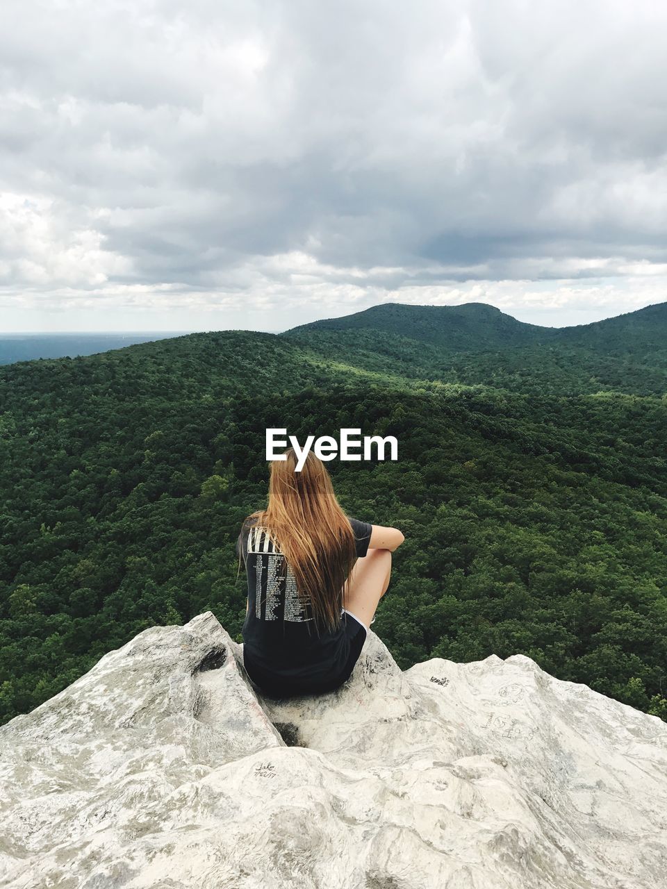 Rear view of woman sitting on cliff against landscape