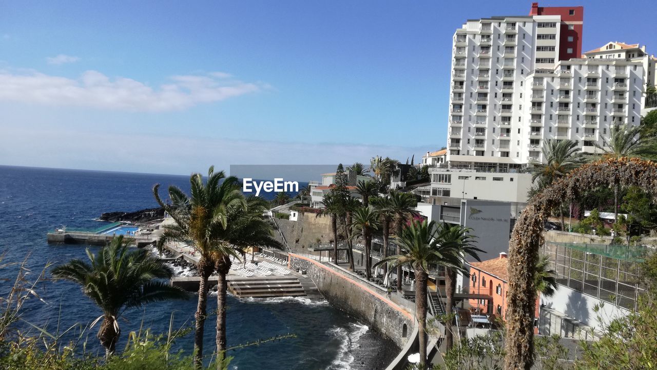 PANORAMIC VIEW OF SWIMMING POOL BY BUILDINGS AGAINST SKY