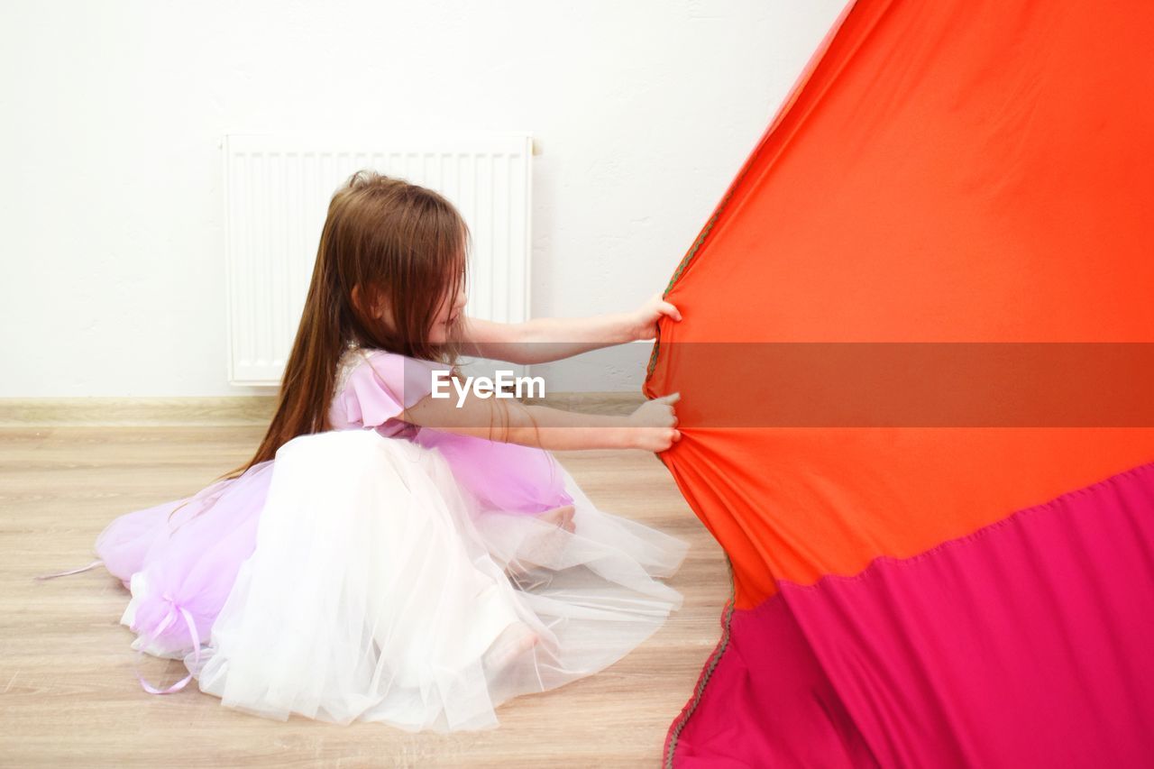 Girl wearing dress pulling textile on hardwood floor at home