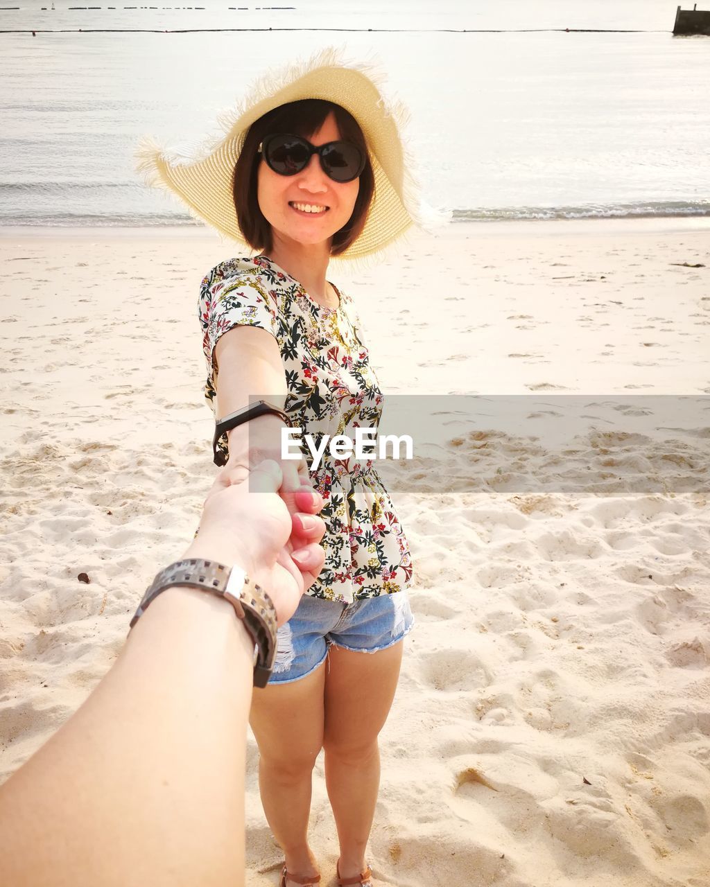 Portrait of woman holding man hand while wearing sunglasses on beach