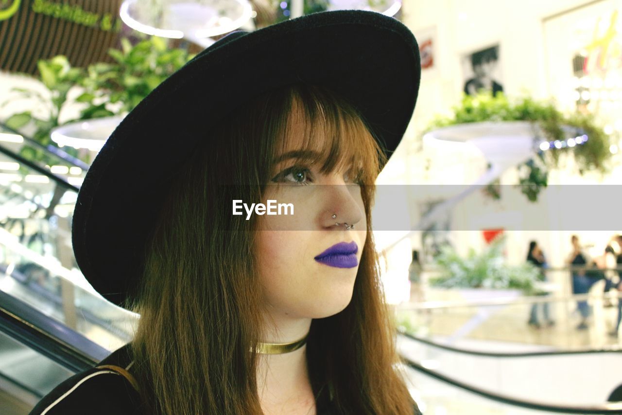 Close-up of woman in purple lipstick with hat looking away